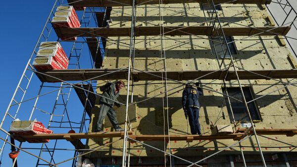Рабочие утепляют фасад строящегося жилого дома 
