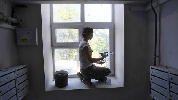 Маляр шпаклюет окно во время ремонта в подъезде жилого дома