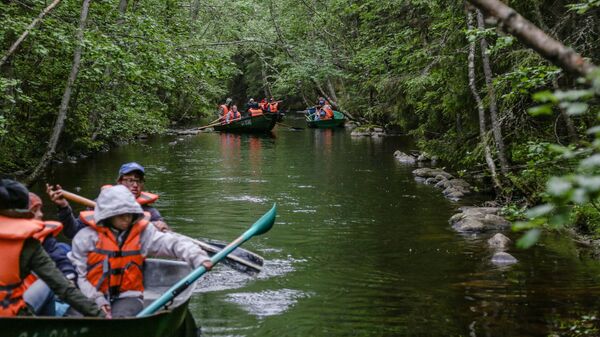 Туристы плывут на лодке вдоль рукотворных каналов между озерами на Соловецких островах