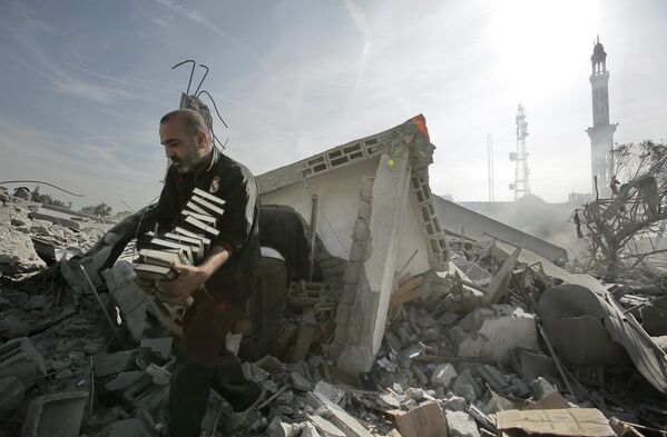 Мужчина выносит стопки Корана из разрушенного взрывом здания в Газе