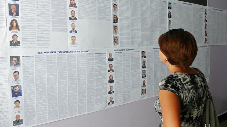 Женщина изучает списки кандидатов на пост депутата в Верховную раду Украины на участке в Черкассах