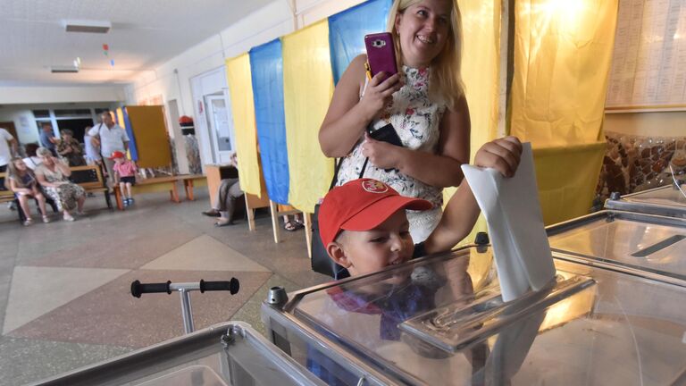 Мальчик опускает бюллетень в урну на избирательном участке во Львове в день досрочных выборов в Верховную раду Украины