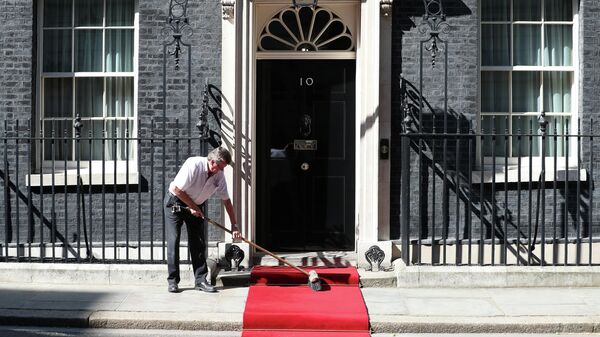 Рабочий подметает красную ковровую дорожку на Даунинг-стрит, 10 в Лондоне