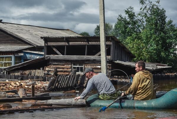 Местные жители плывут на лодке по  затопленной улице в Амурской области
