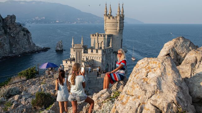 Отдыхающие фотографируются возле замка Ласточкино гнездо на береговой скале в поселке Гаспра в Крыму