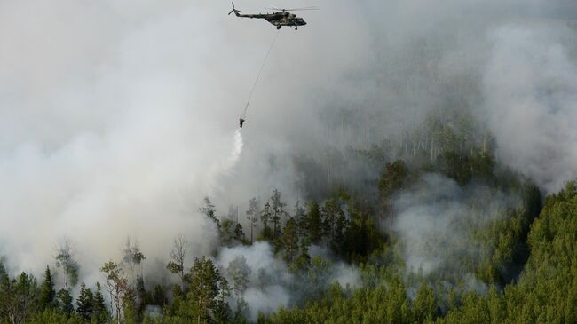Вертолет Ми-8 с водосливной системой для забора воды в открытых водоемах во время тушения лесных пожаров в Богучанском районе Красноярского края