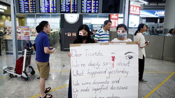 Участники акции протеста в аэропорту Гонконга с плакатом с извинениями перед туристами