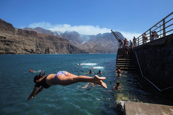 Люди купаются недалеко от очага лесного пожара на побережье Агаэте на острове Гран-Канария, Испания