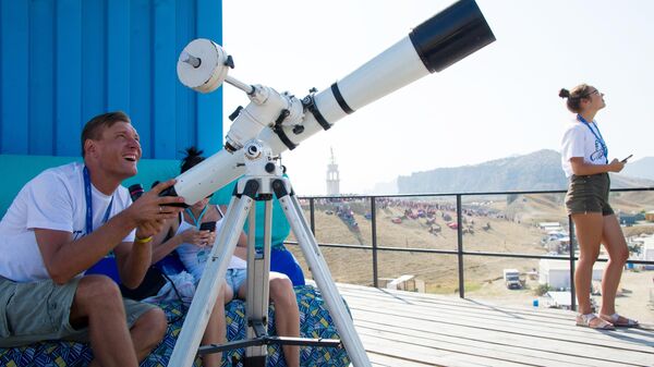 Зрители наблюдают через любительский телескоп за показательными выступлениями авиации в небе над площадкой фестиваля творческих сообществ Таврида-АРТ в бухте Капсель в Судаке