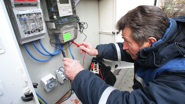 Электрик осуществляет проверку общедомового прибора учета потребления электроэнергии в одном из жилых домов