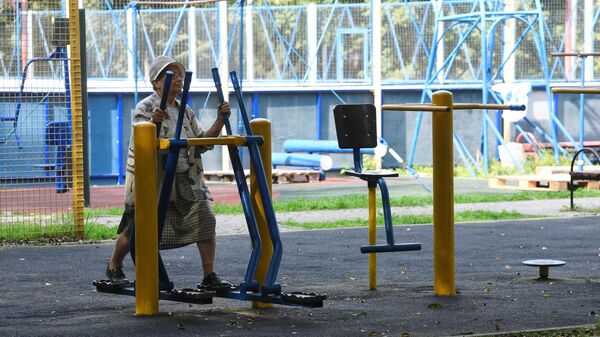 Пожилая женщина занимается на благоустроенной спортивной площадке 