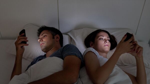 Молодая пара в кровати со смартфонами