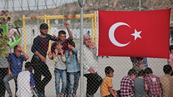 Мигранты стоят за забором в лагере беженцев Низип в провинции Газиантеп, на юго-востоке Турции