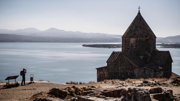 Турист фотографирует монастырь Севанаванк, расположенный на северо-западном побережье озера Севан в провинции Гехаркуник в Армении