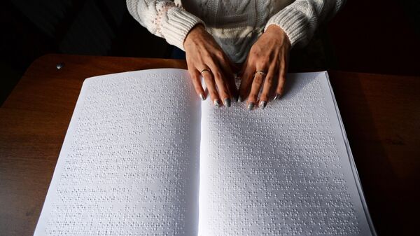 Незрячая женщина читает с помощью рук книгу, в которой использован шрифт Брайля 