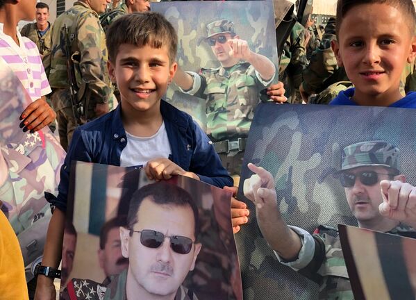 Дети с плакатами с портретом президента Сирии Башара Асада в освобожденном сирийской правительственной армией городе Манбидж в Сирии