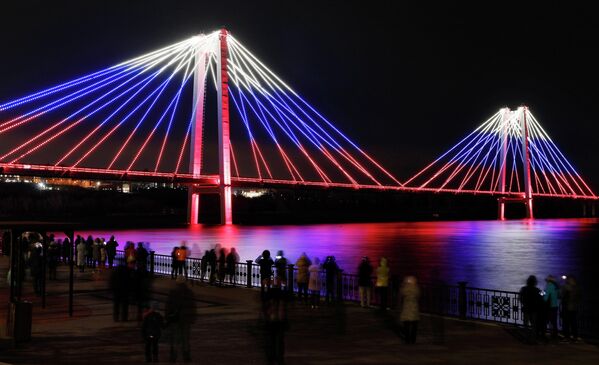 Зрители смотрят на окрашенный в цвета российского государственного флага Виноградовский пешеходный мост в Красноярске 