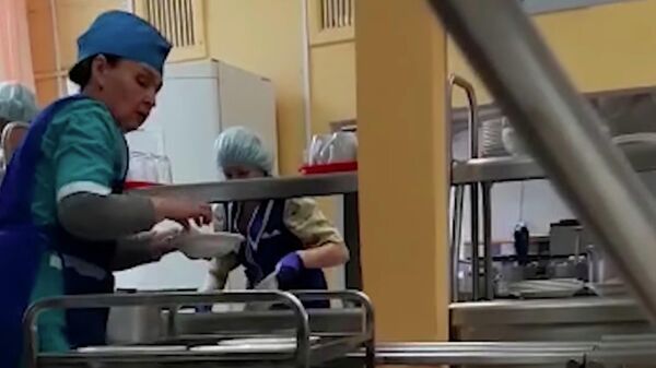 Стоп-кадр видео, на котором в школьной столовой еду раскладывают по тарелкам руками