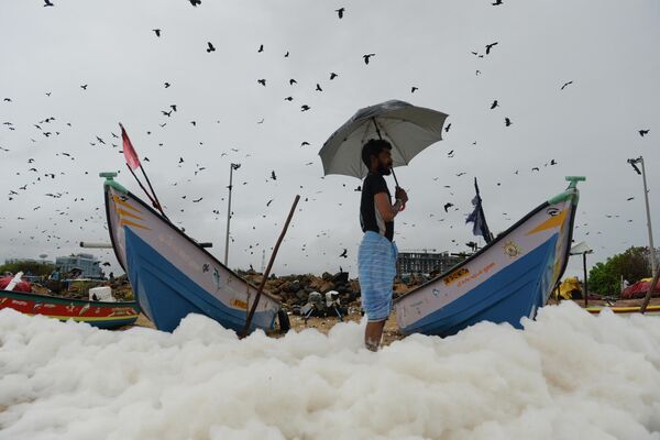 Мужчина среди пенистых выделений, вызванных загрязнением, на пляже Марина в Ченнае, Индия