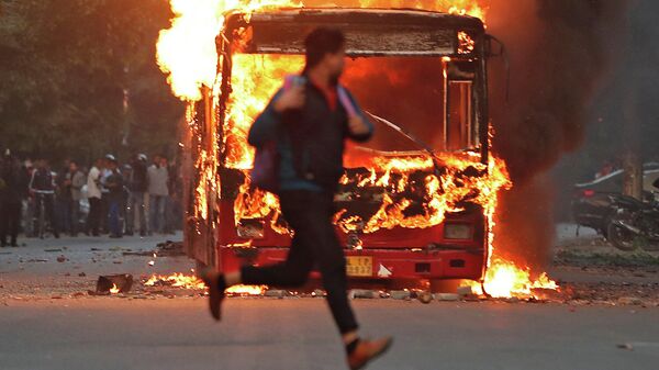 Мужчина пробегает мимо горящего автобуса, который был подожжен демонстрантами во время протеста против нового закона в Нью-Дели, Индия. 15 декабря 2019 года