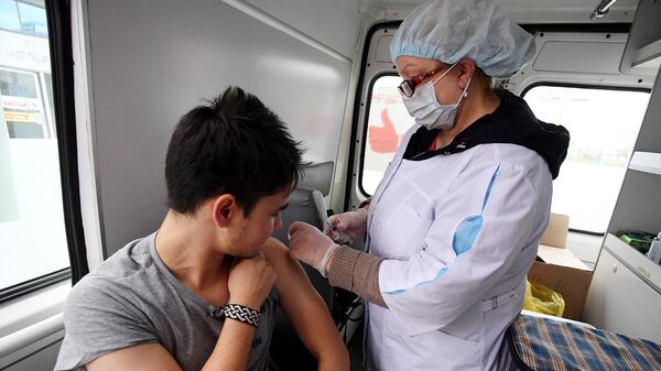 Сотрудник пункта вакцинации делает мужчине прививку