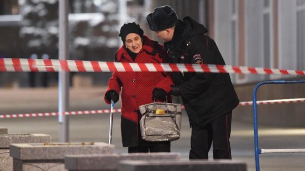 Сотрудник полиции помогает женщине пройти в зоне оцепления недалеко от здания ФСБ на Лубянской площади в Москве, где произошла стрельба