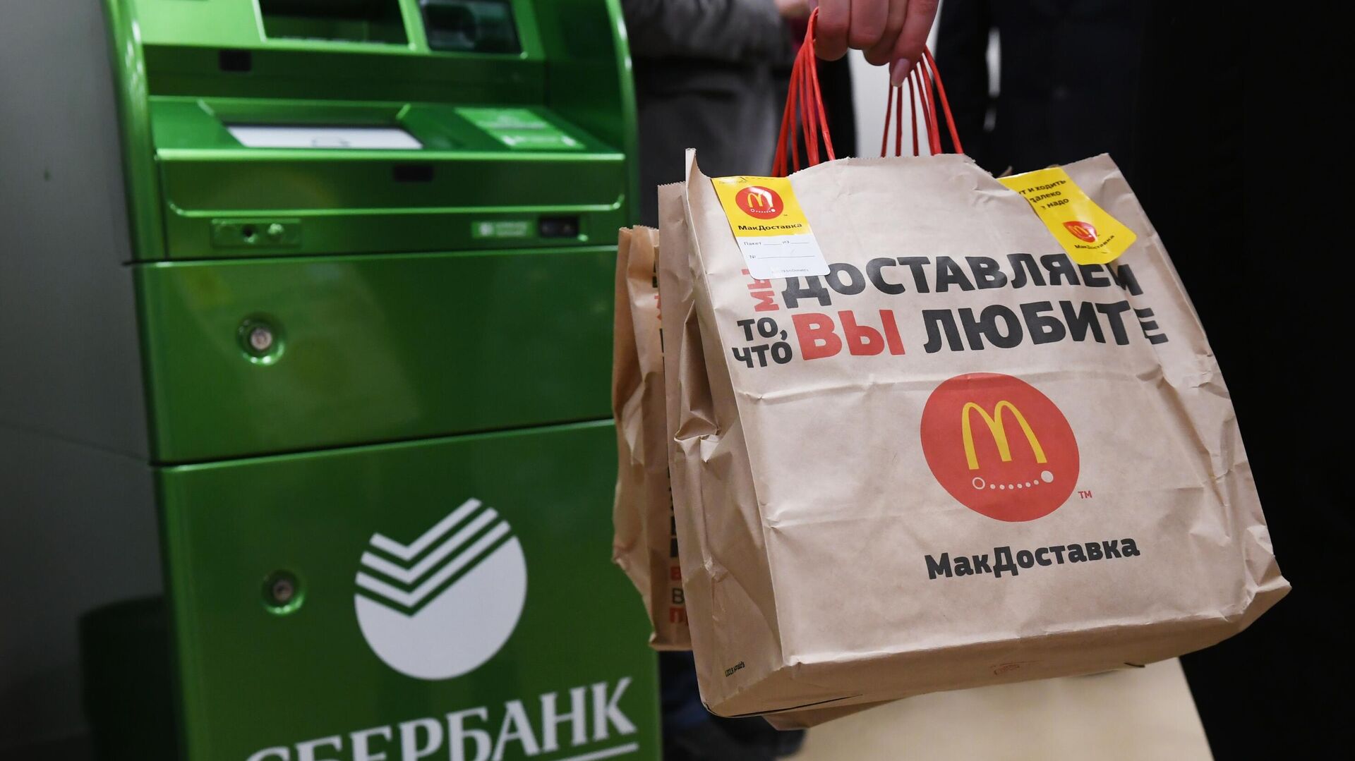 Посетитель совместного отделения Сбербанка и McDonalds в Москве стоит у банкомата с пакетами Макдоставки - РИА Новости, 1920, 03.02.2022