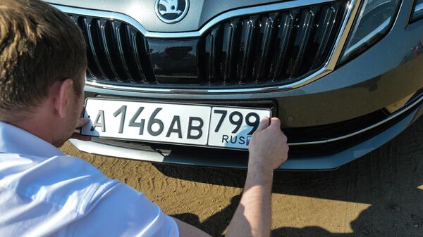 Автовладелец устанавливает номерной знак на автомобиль 