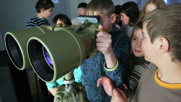 Школьники смотрят в бинокуляр во время экскурсии в планетарий