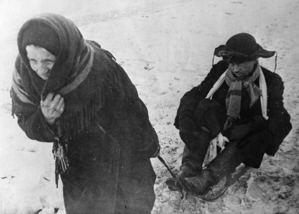 Жители блокадного Ленинграда: женщина везет ослабевшего от голода мужа на санках