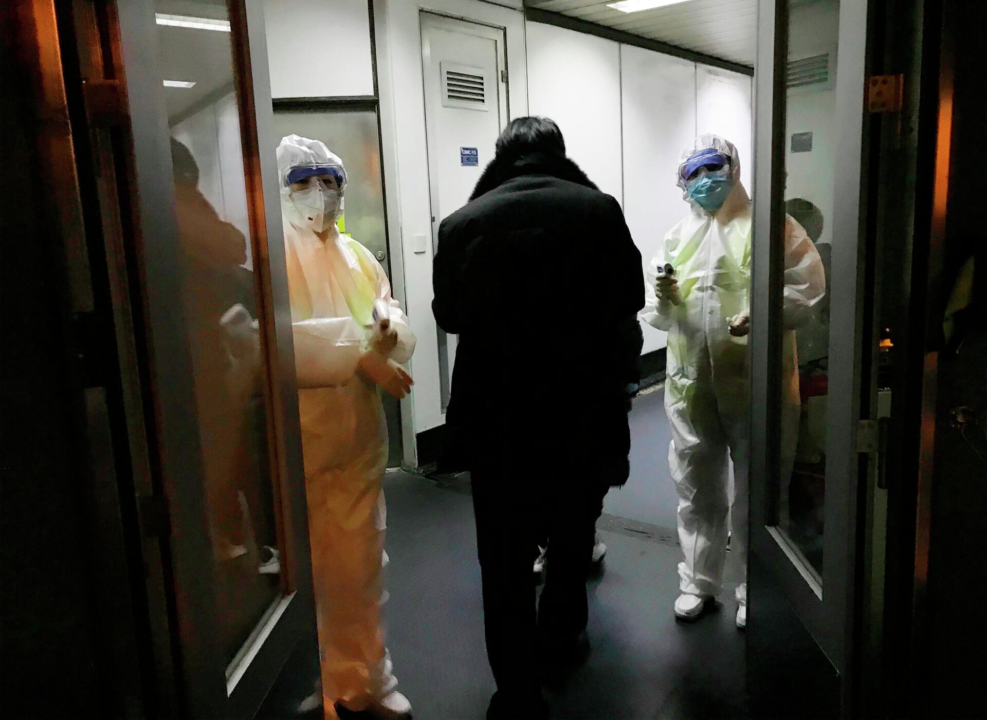 Медицинские работники в спецкостюмах проверяют температуру тела пассажиров, прибывающих из города Ухань в аэропорту Пекина - РИА Новости, 1920, 27.10.2020