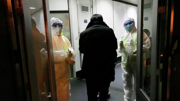 Медицинские работники в спецкостюмах проверяют температуру тела пассажиров, прибывающих из города Ухань в аэропорту Пекина