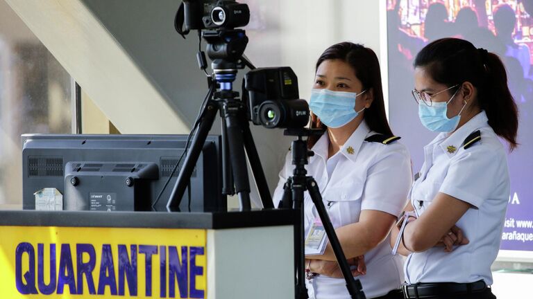 Сотрудники аэропорта следят за тепловым сканером в международном аэропорту Манила имени Ниноя Акино