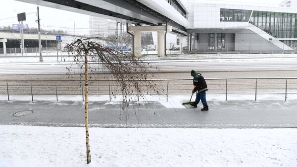 Сотрудник коммунальной службы чистит тротуар от снега в Москве