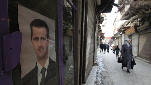 Жительница Дамаска проходит мимо здания с портретом президента Сирии Башара Асада.