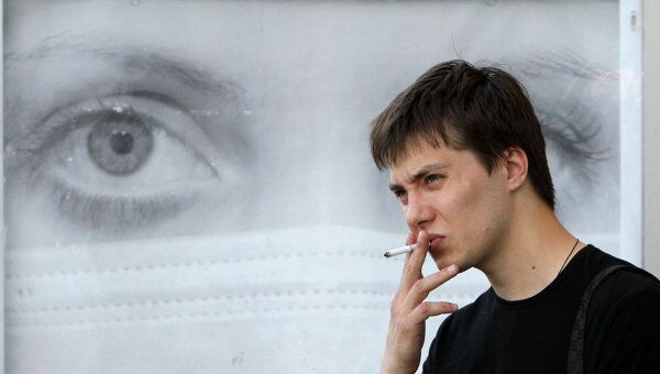 Молодой человек курит у рекламного щита на одной из улиц Москвы. Архив