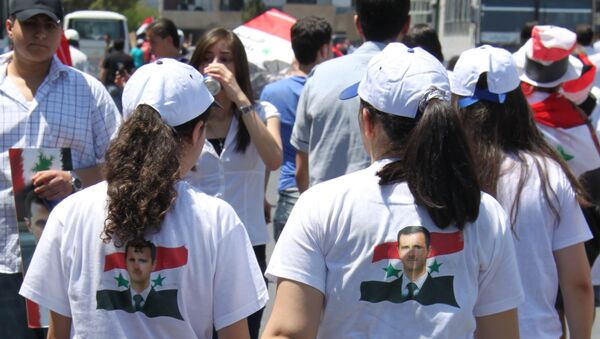 Девушки в Дамаске в футболках с изображением Башара Асада на фоне флага Сирии