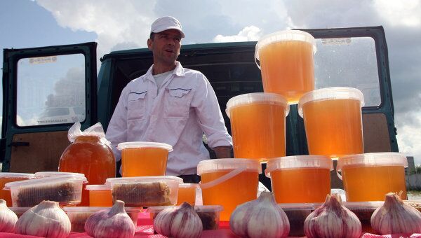 Торговец продает мед и чеснок на ярмарке продовольственных товаров