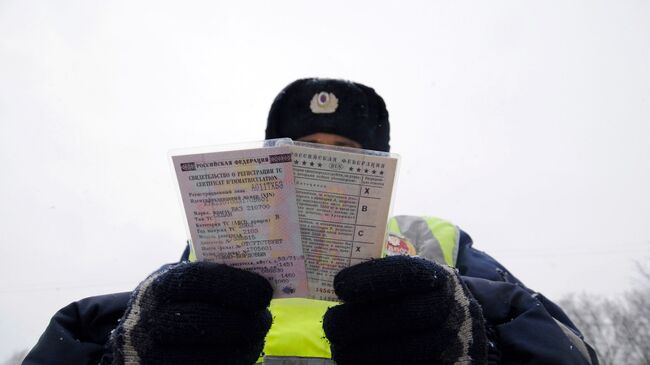 Сотрудник дорожно-патрульной службы ГИБДД держит в руках права и ПТС