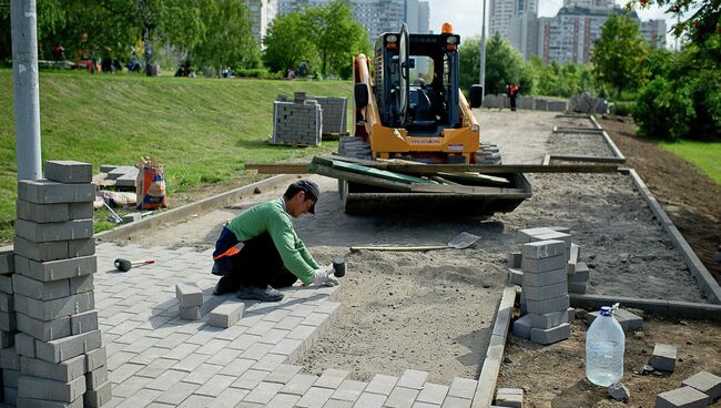 Рабочий укладывает тротуарную плитку. Архив