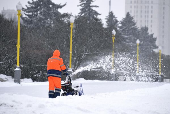 Сотрудник коммунальной службы убирает снег с помощью снегоуборочной машины возле здания МГУ на Воробьевых горах в Москве
