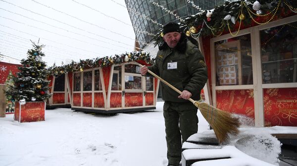 Мужчина убирает снег на площадке фестиваля Путешествие в Рождество в Москве