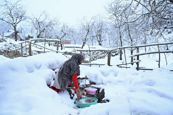 Женщина моет посуду после снегопада на окраине Сринагара в Индии