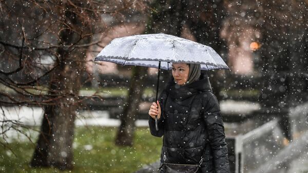 Женщина идет с зонтом во время снегопада в Москве
