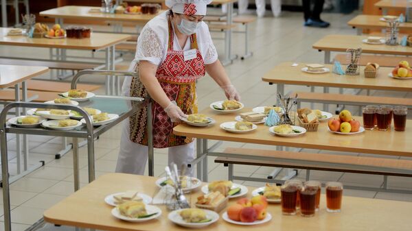 Работница школьной столовой разносит тарелки с едой к обеду учеников