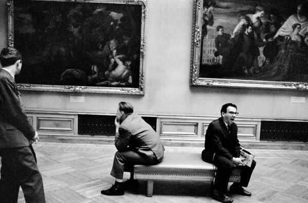 Посетители музея отдыхают, сидя на банкетке в зале