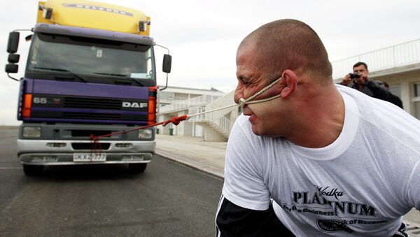 Борец Лаша Патарая пытается сдвинуть грузовик с помощью привязанной к уху веревки. Архив
