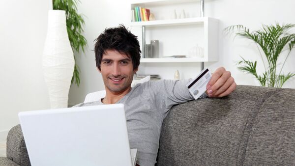 Мужчина средних лет за компьютером держит кредитную карту в руках и улыбается