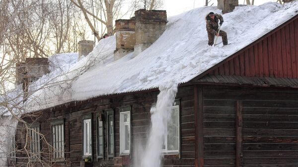 Коммунальщики счищают снег с крыши дома. Архивное фото