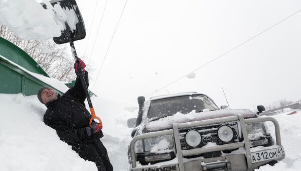 Мужчина очищает снег вокруг своего автомобиля после сильного снегопада в Петропавловске-Камчатском